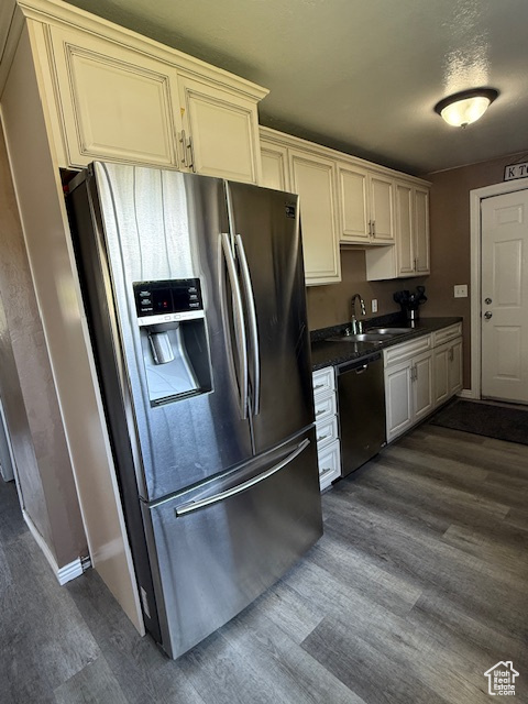 Kitchen featuring stainless steel appliances, dark wood finished floors, dark countertops, and cream cabinetry