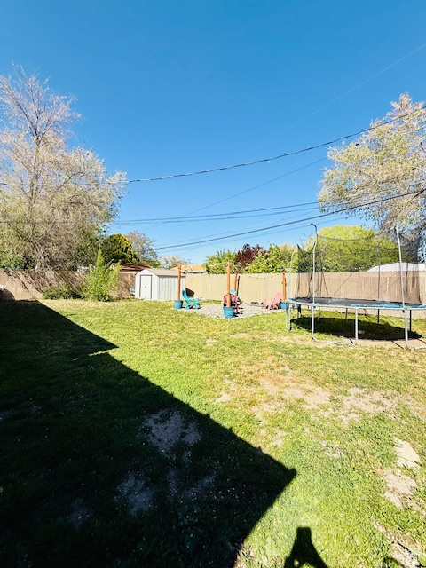 View of yard featuring a storage unit, a fenced backyard, a trampoline, and an outdoor structure