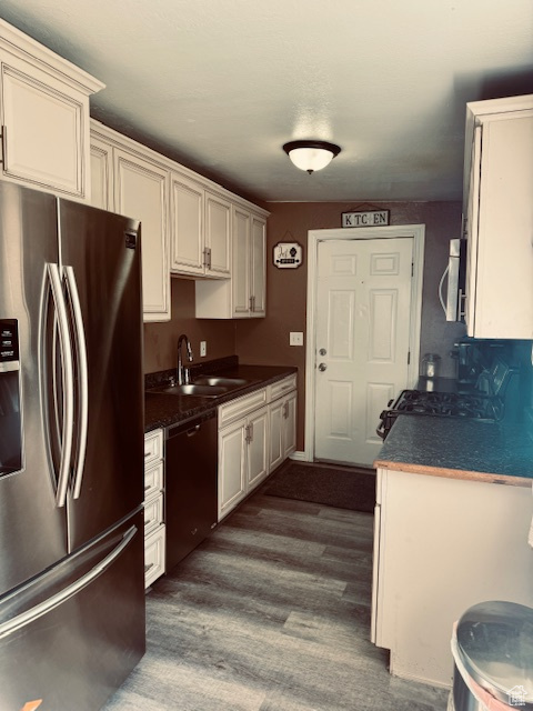Kitchen featuring dark countertops, dishwasher, gas stove, a sink, and stainless steel fridge