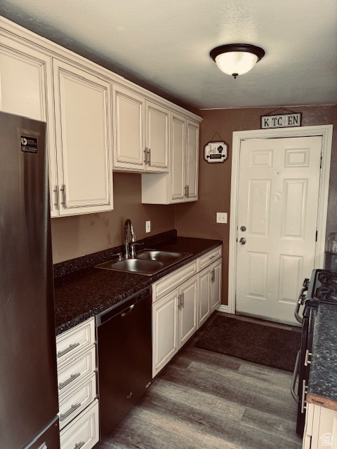 Kitchen featuring gas range, dark countertops, a sink, freestanding refrigerator, and dishwashing machine