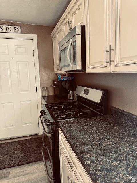 Kitchen with a textured wall, appliances with stainless steel finishes, and dark stone countertops