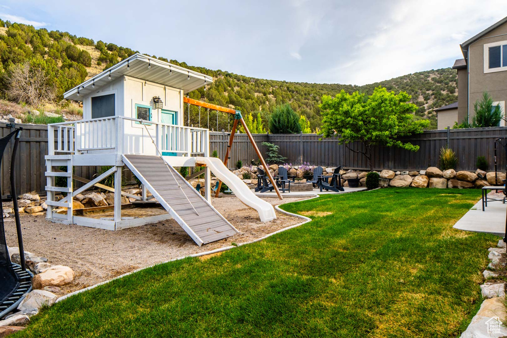 View of play area with a fenced backyard, an outdoor fire pit, a mountain view, and a patio
