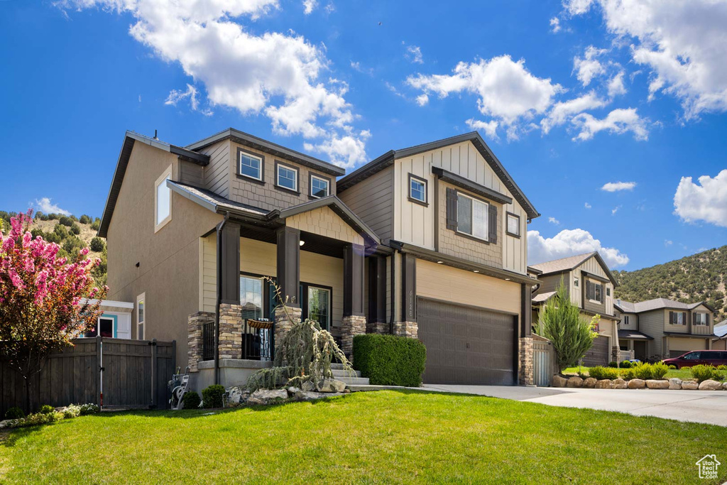 Craftsman-style home featuring fence, a front lawn, stone siding, a garage, and concrete driveway