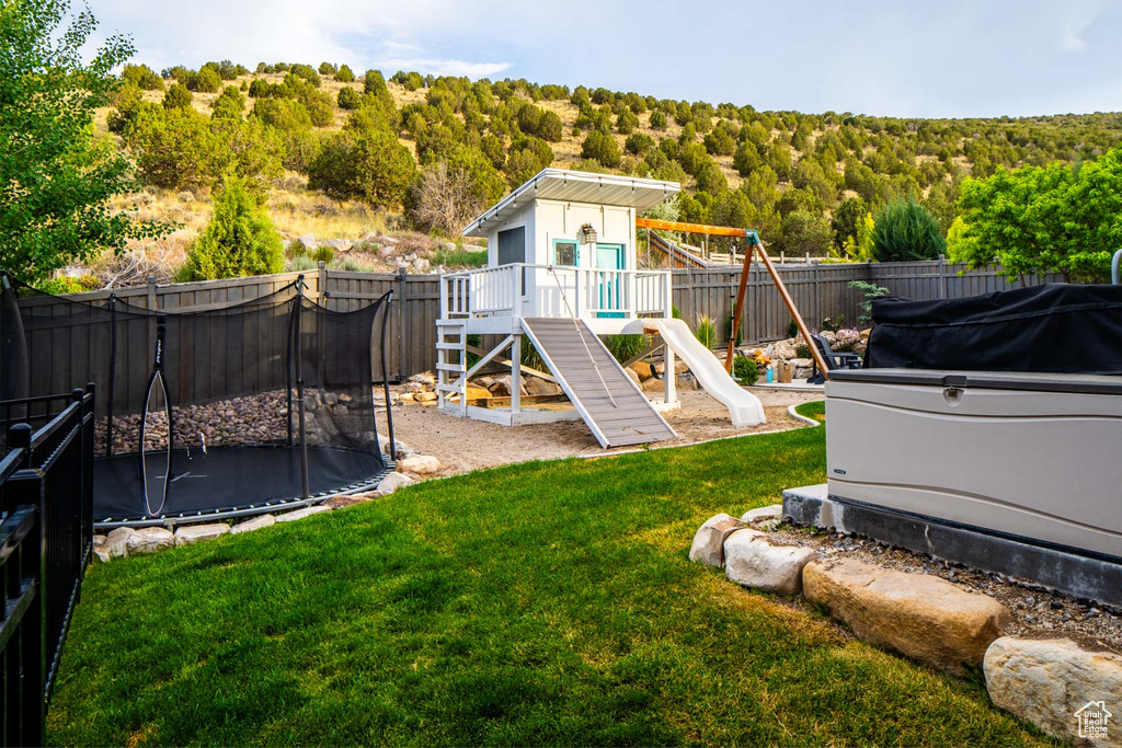 Fenced backyard featuring a trampoline, a playground, and a forest view