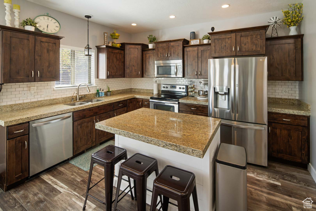 Kitchen with appliances with stainless steel finishes, decorative backsplash, a sink, and dark wood-type flooring