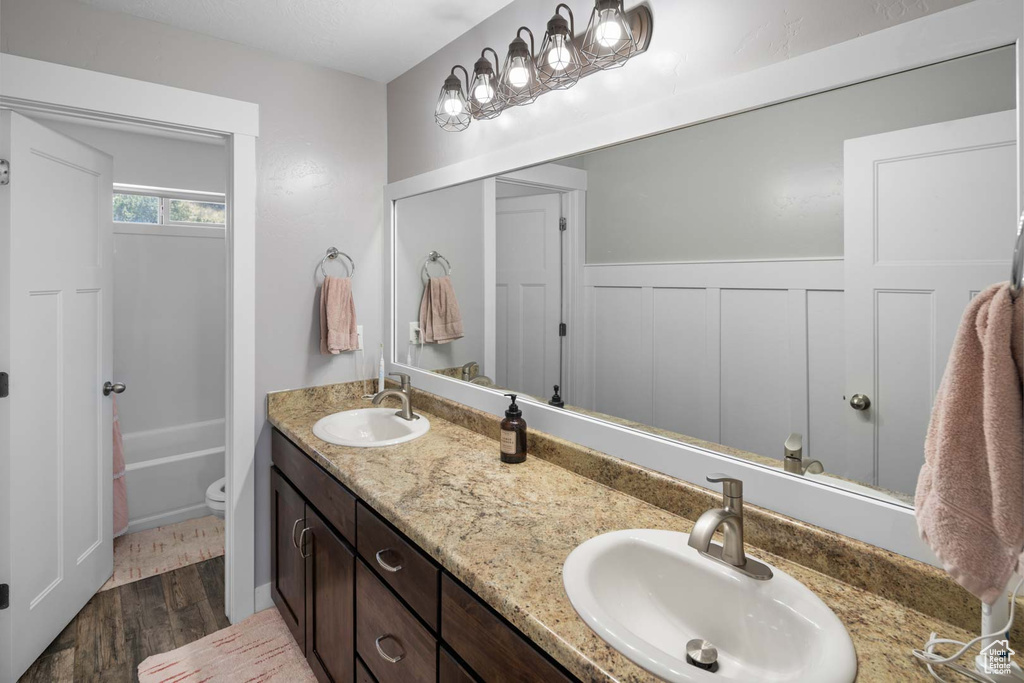 Full bath with a sink, double vanity, toilet, and wood finished floors