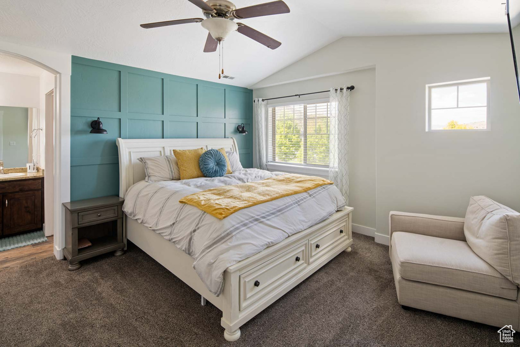 Bedroom with arched walkways, vaulted ceiling, dark carpet, and connected bathroom