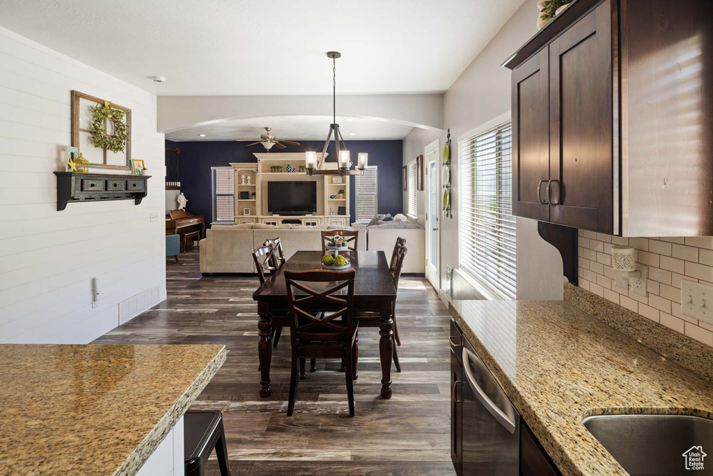Dining space featuring arched walkways, ceiling fan with notable chandelier, and dark wood-style flooring