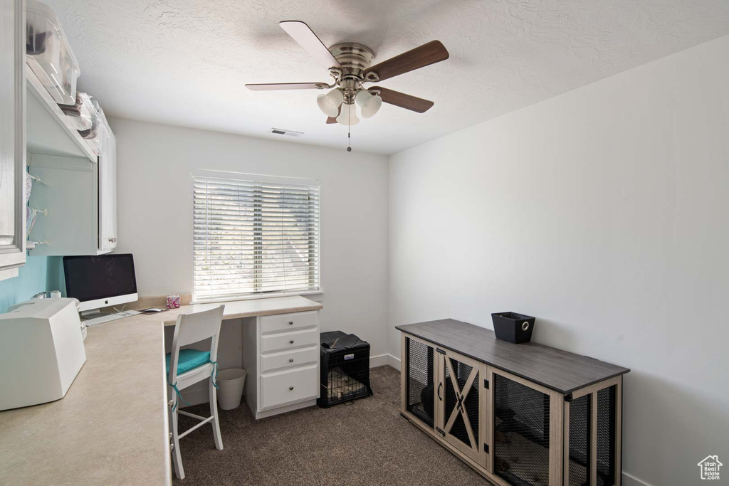 Office space with ceiling fan, visible vents, and dark colored carpet