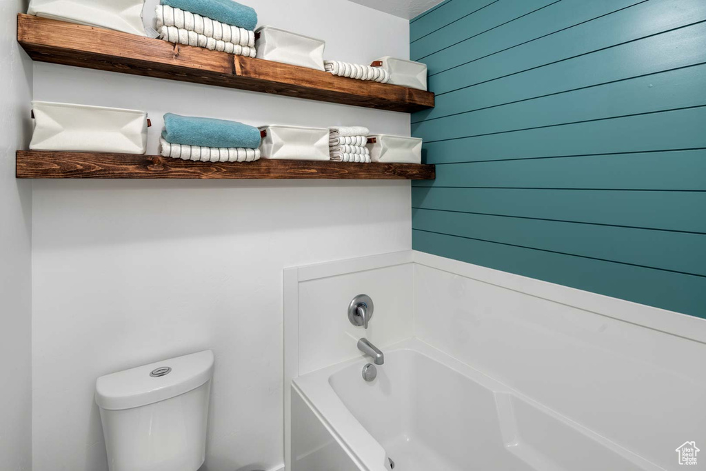 Full bath with wooden walls, toilet, and a bath