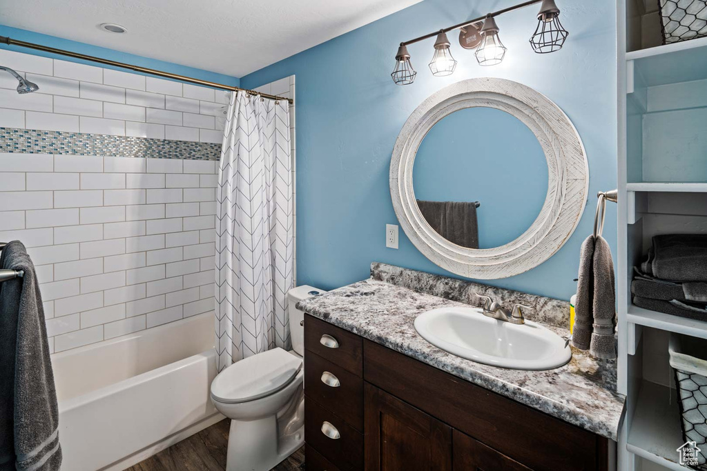 Bathroom featuring toilet, shower / bath combination with curtain, wood finished floors, and vanity