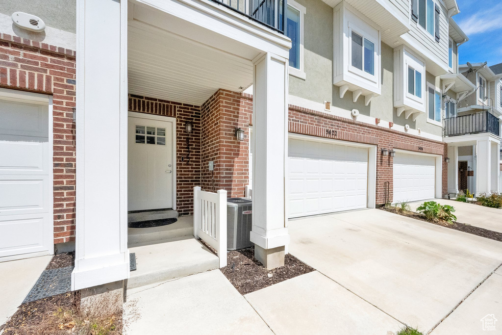 View of exterior entry featuring a garage, central AC, driveway, and brick siding