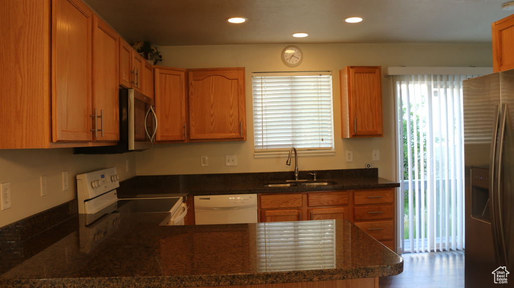 Kitchen with appliances with stainless steel finishes, a sink, dark stone countertops, a peninsula, and recessed lighting