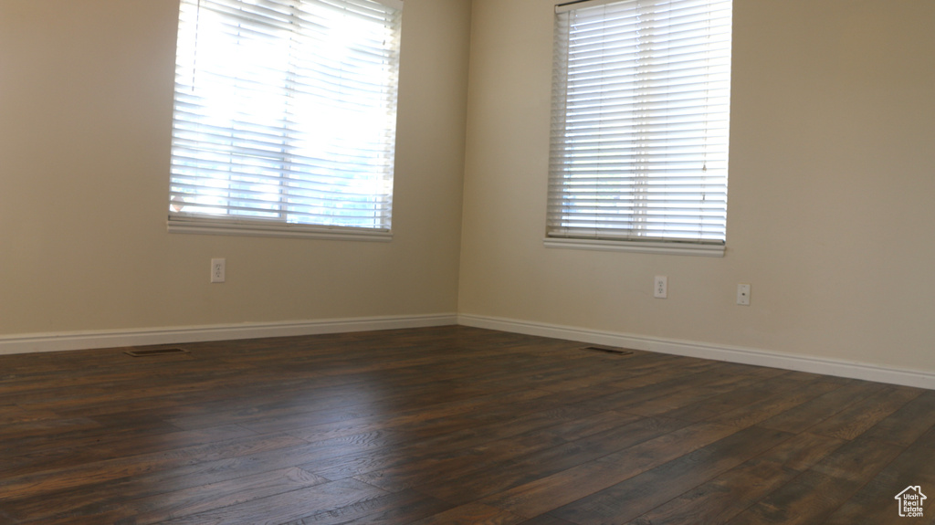 Unfurnished room with baseboards, dark wood finished floors, and visible vents