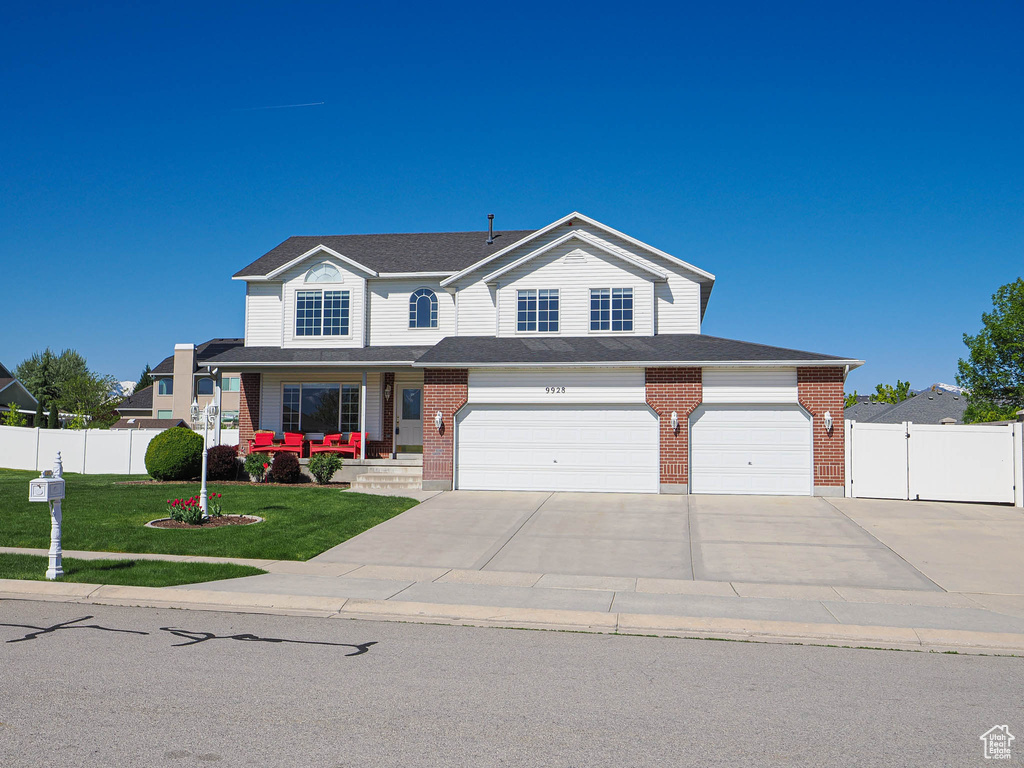 View of front of property with concrete driveway, brick siding, fence, and a front lawn