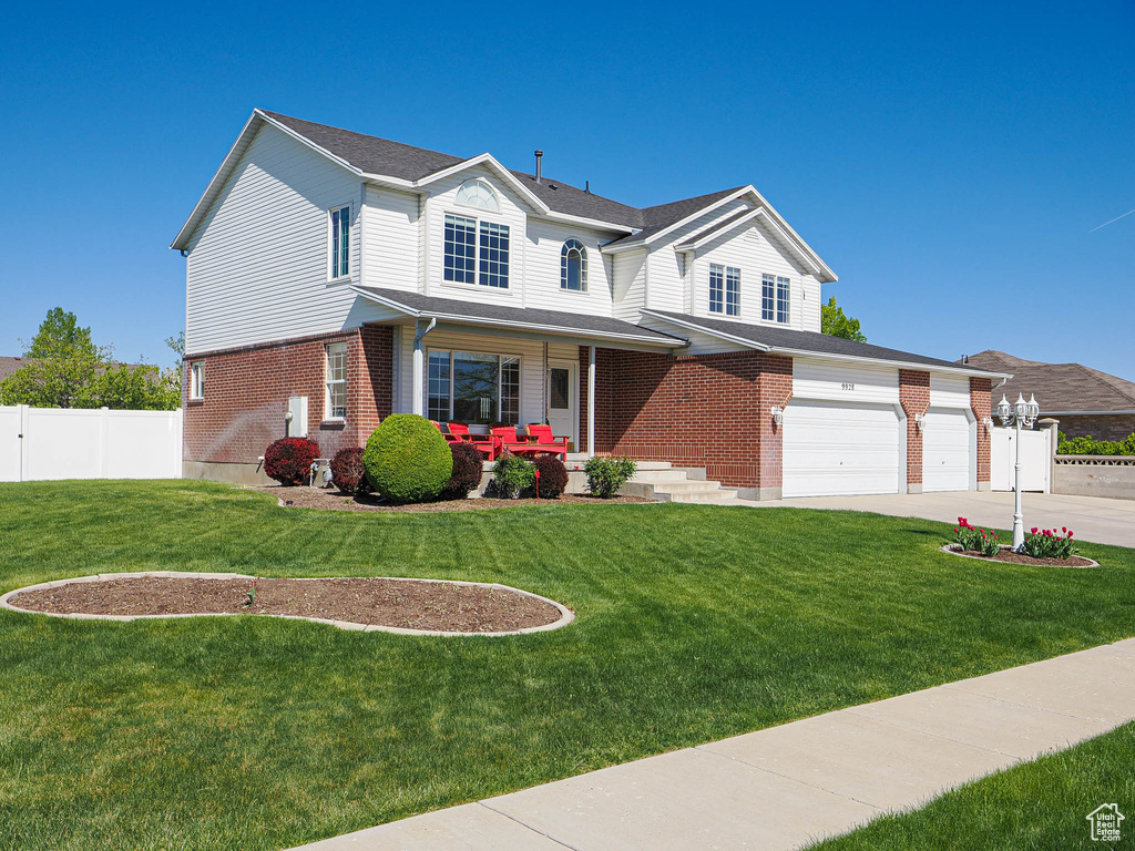 View of front of house featuring covered porch, a front yard, brick siding, fence, and concrete driveway