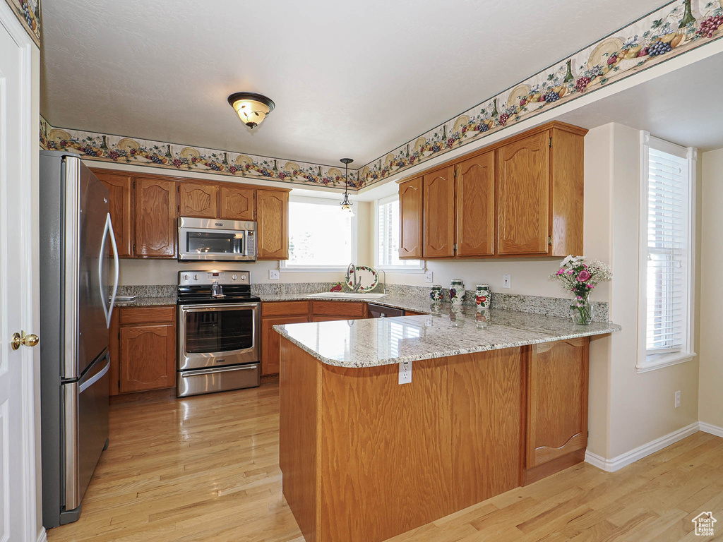 Kitchen featuring light wood finished floors, a peninsula, brown cabinets, and stainless steel appliances