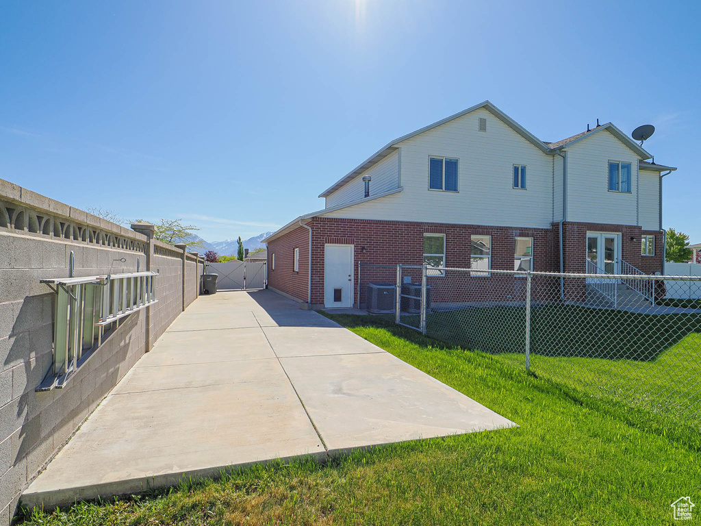 Back of property featuring central AC, a fenced backyard, brick siding, a gate, and a yard