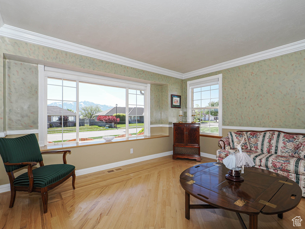 Living room with visible vents, ornamental molding, light wood-style floors, and wallpapered walls