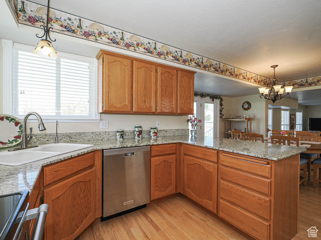 Kitchen featuring hanging light fixtures, a sink, light wood finished floors, a peninsula, and stainless steel dishwasher