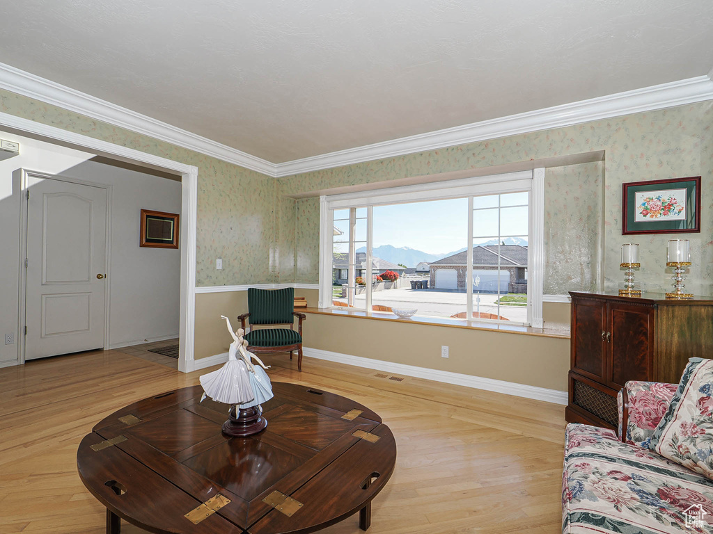 Living room featuring light wood-style floors, ornamental molding, wallpapered walls, and visible vents