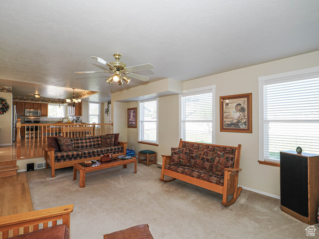 Living room featuring baseboards, ceiling fan with notable chandelier, a wealth of natural light, and light colored carpet