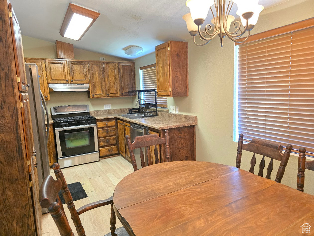Kitchen featuring lofted ceiling, under cabinet range hood, a sink, a notable chandelier, and stainless steel appliances