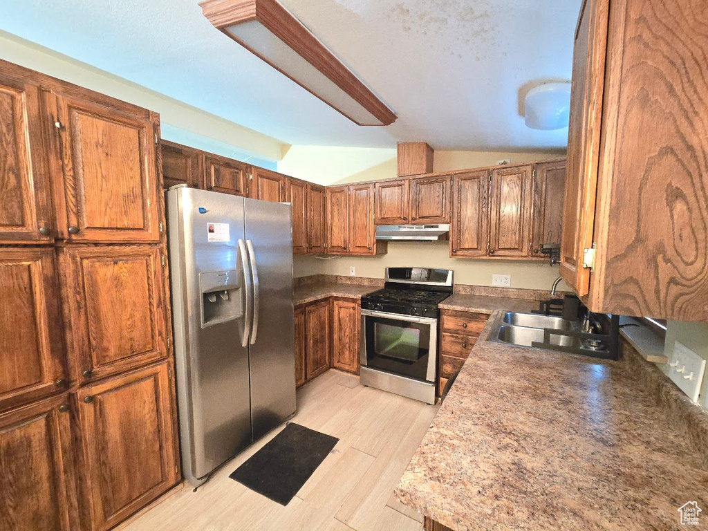 Kitchen featuring brown cabinets, appliances with stainless steel finishes, a sink, under cabinet range hood, and vaulted ceiling