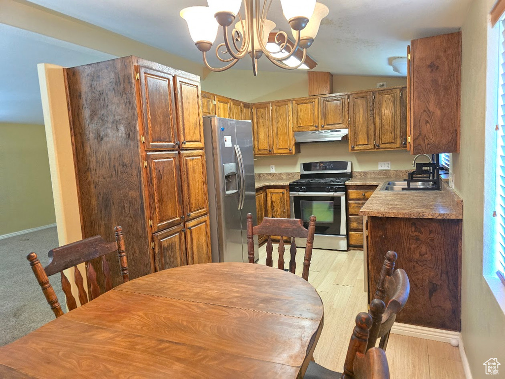 Kitchen featuring under cabinet range hood, lofted ceiling, a sink, a notable chandelier, and stainless steel appliances