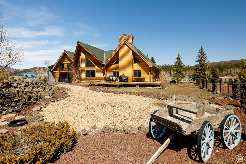 Rear view of house featuring a chimney, fence, log exterior, and a deck