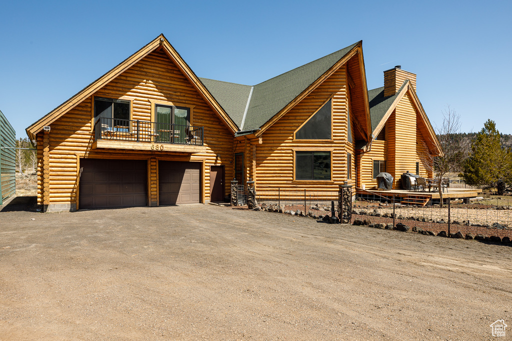 Log-style house featuring a garage, log siding, a chimney, and aphalt driveway
