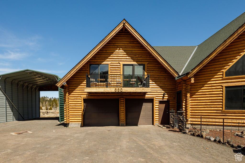 Log-style house featuring driveway, log exterior, a balcony, and a detached carport