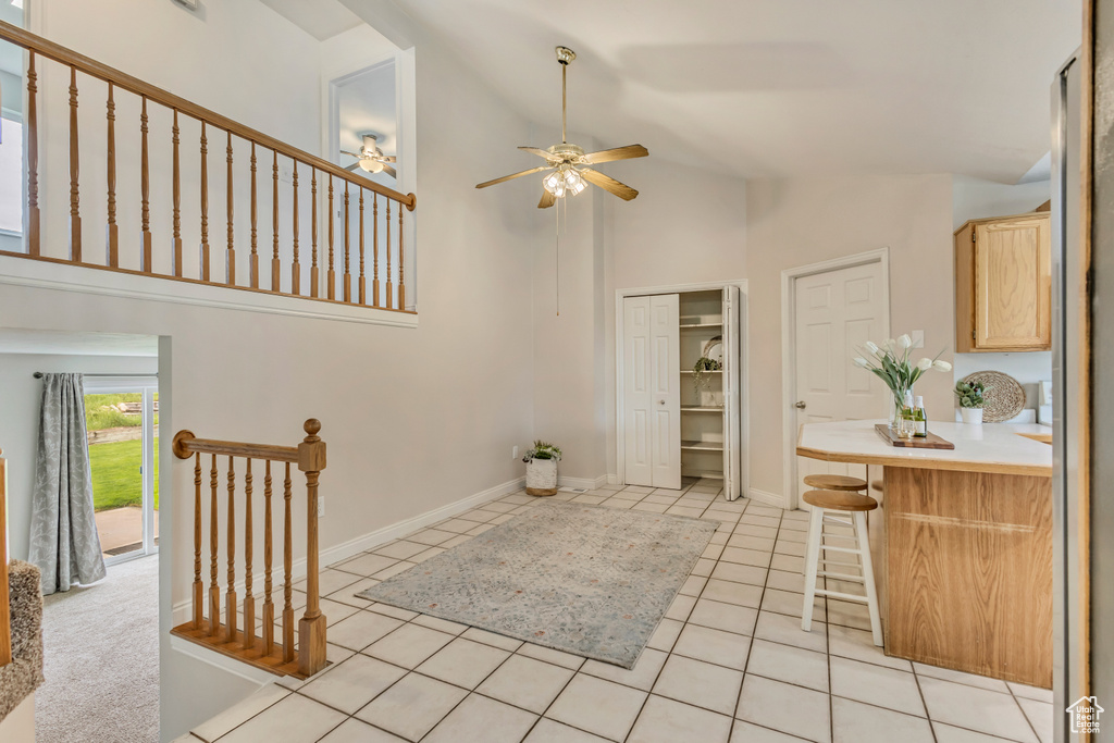 Interior space featuring baseboards, a ceiling fan, high vaulted ceiling, and light tile patterned floors