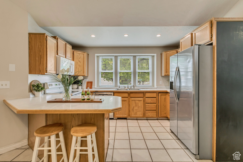Kitchen featuring electric range, light tile patterned floors, stainless steel fridge with ice dispenser, white microwave, and a peninsula