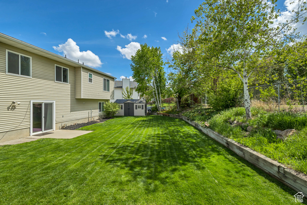 View of yard featuring a storage shed, fence, an outdoor structure, and a patio area