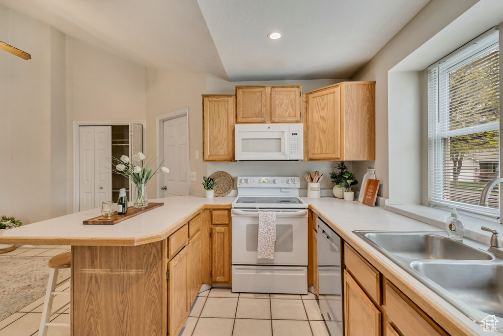 Kitchen with a peninsula, light countertops, white appliances, and a sink