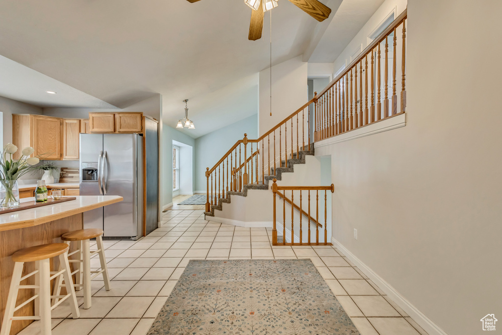 Kitchen featuring light brown cabinetry, light tile patterned flooring, stainless steel fridge, light countertops, and ceiling fan with notable chandelier