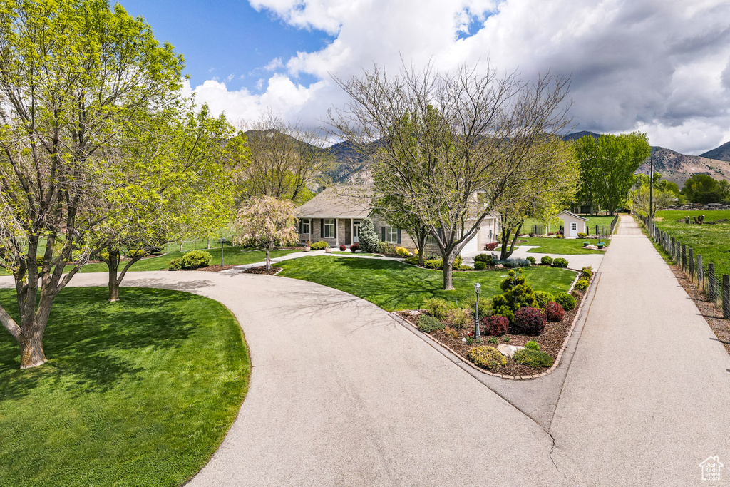 View of property's community with curved driveway, a mountain view, a yard, and fence