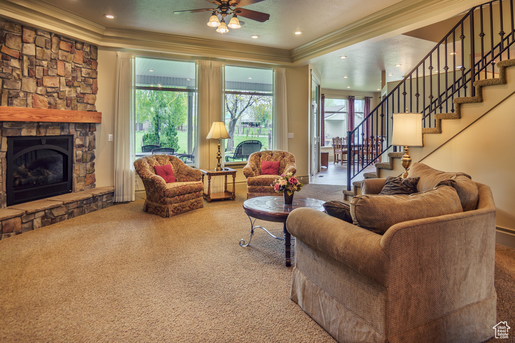 Living area with crown molding, a ceiling fan, a stone fireplace, and stairs