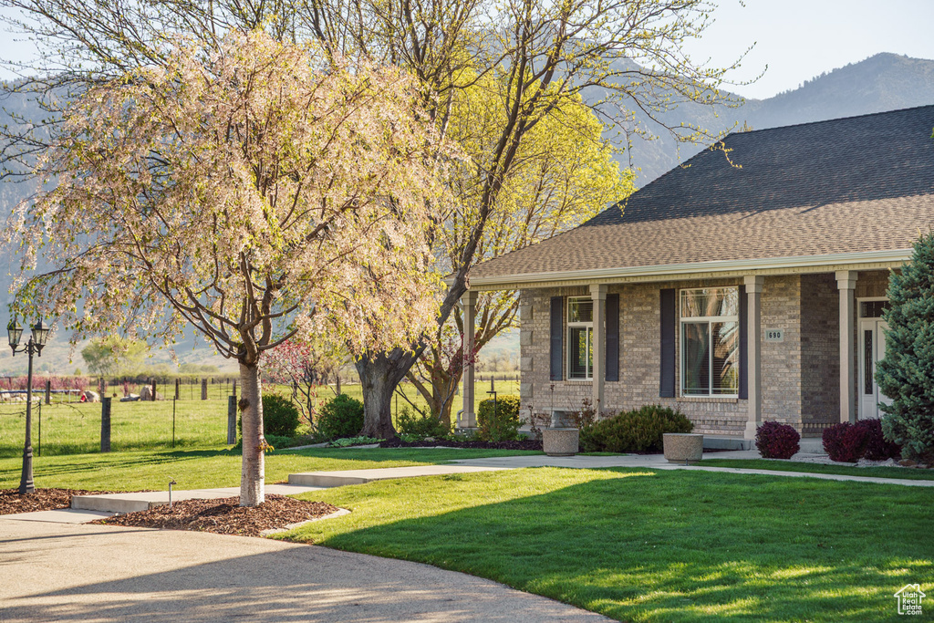View of side of property featuring covered porch, brick siding, a shingled roof, a lawn, and a mountain view