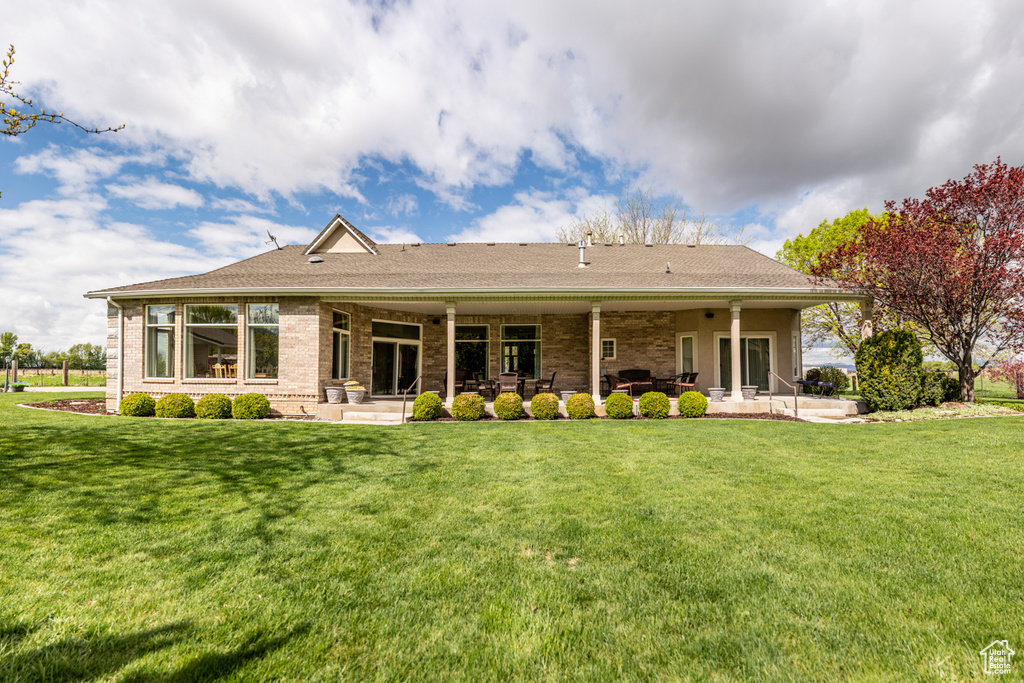 Back of property with a lawn, brick siding, a shingled roof, and a patio area