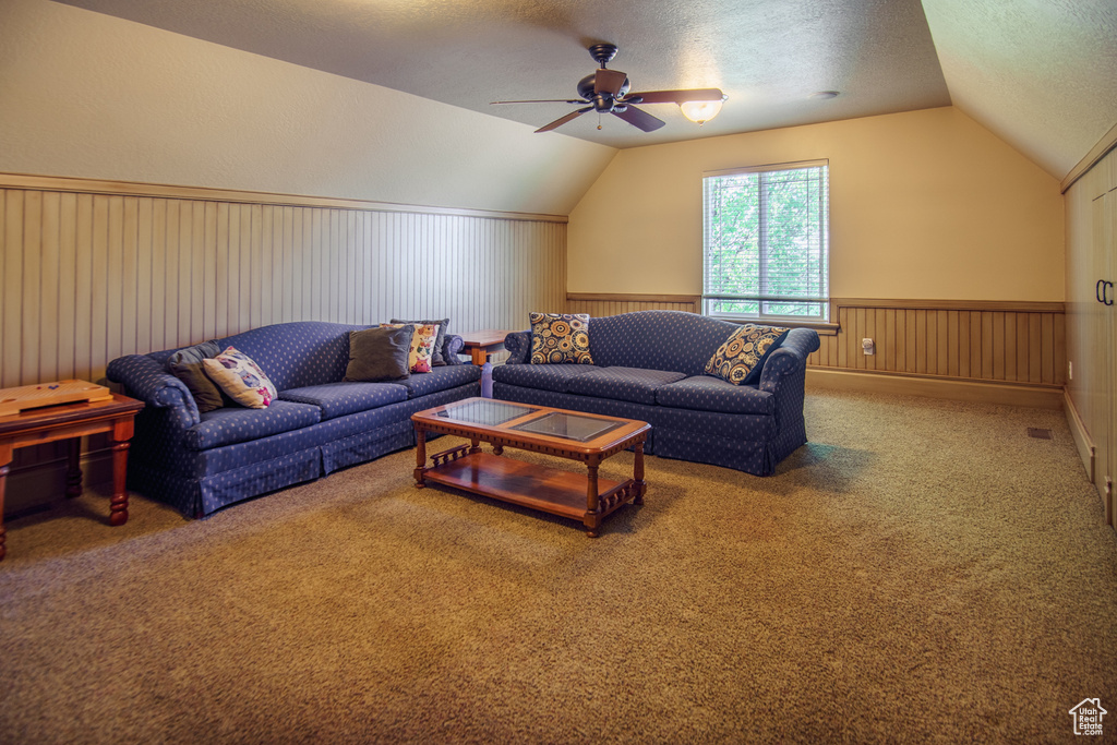 Living room with vaulted ceiling, a ceiling fan, carpet flooring, and a textured ceiling