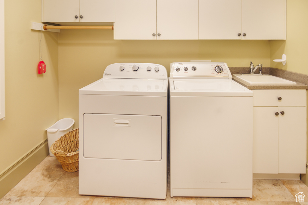 Laundry room with cabinet space, baseboards, washing machine and dryer, and a sink