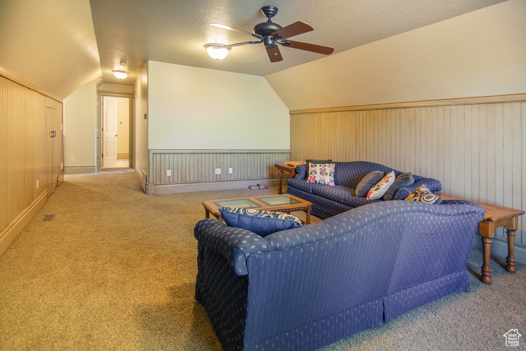 Carpeted living room featuring a ceiling fan, a textured ceiling, vaulted ceiling, and wainscoting
