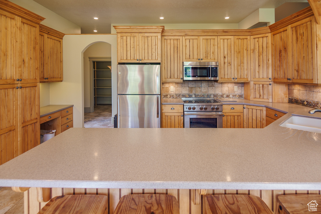 Kitchen with decorative backsplash, appliances with stainless steel finishes, arched walkways, a sink, and a breakfast bar