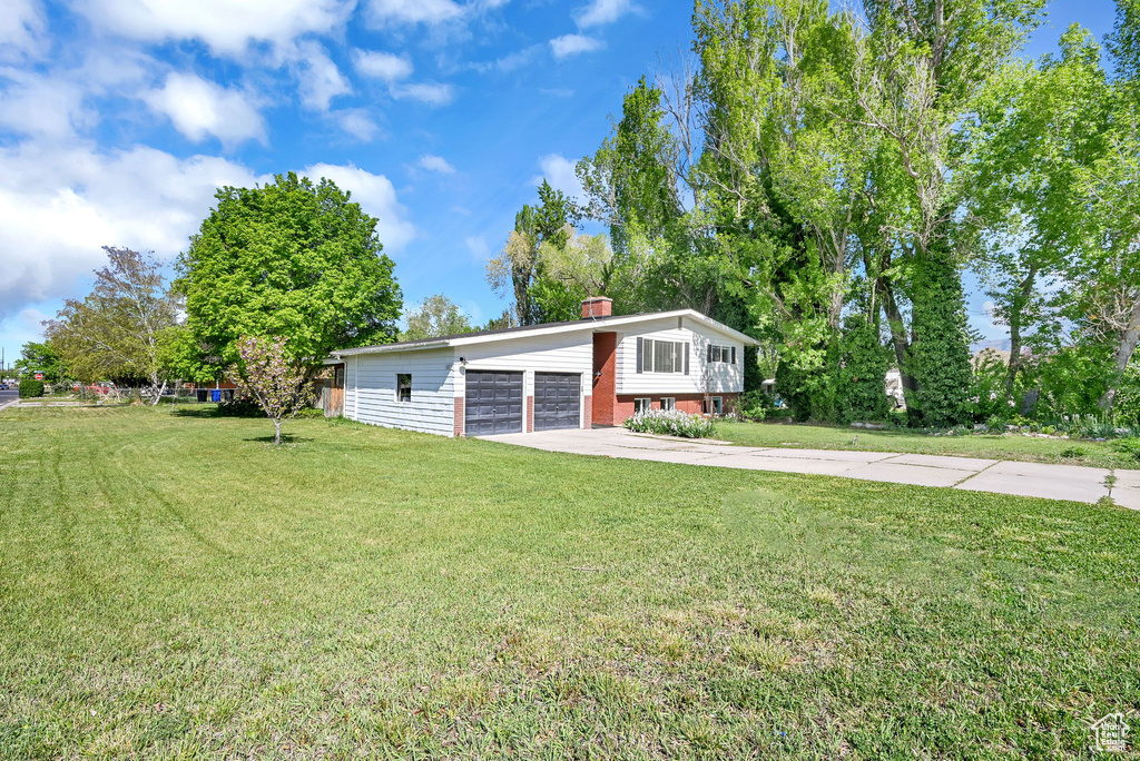Raised ranch featuring a chimney, a front yard, and a detached garage