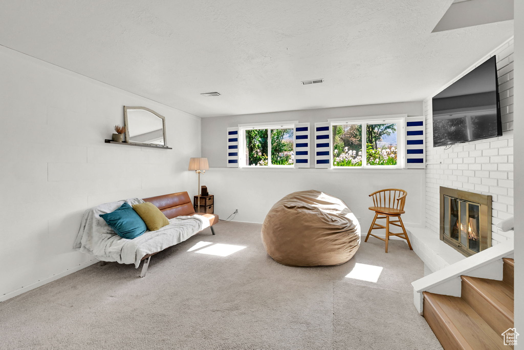 Living area featuring visible vents, carpet flooring, a textured ceiling, and a brick fireplace