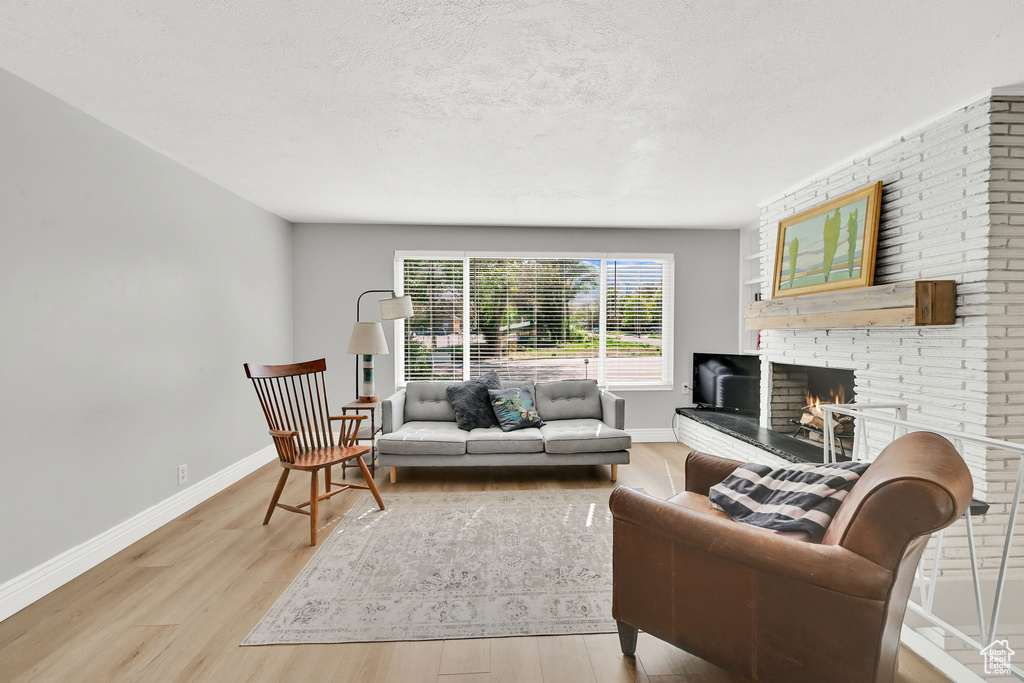 Living room featuring baseboards, a textured ceiling, light wood-style flooring, and a brick fireplace