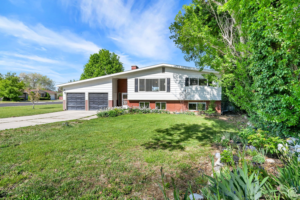 Bi-level home with an attached garage, a chimney, driveway, and a front lawn