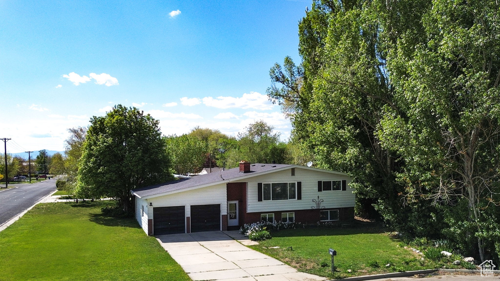 View of front of house with an attached garage, a front lawn, a chimney, and concrete driveway